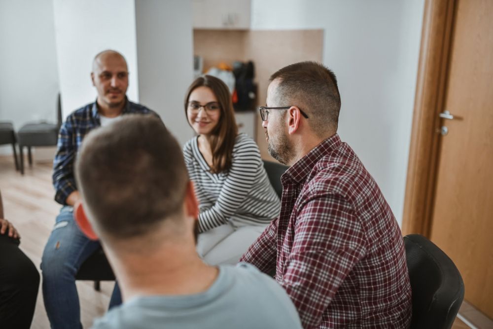 Four people sit in a circle in a room, talking and smiling at each other.