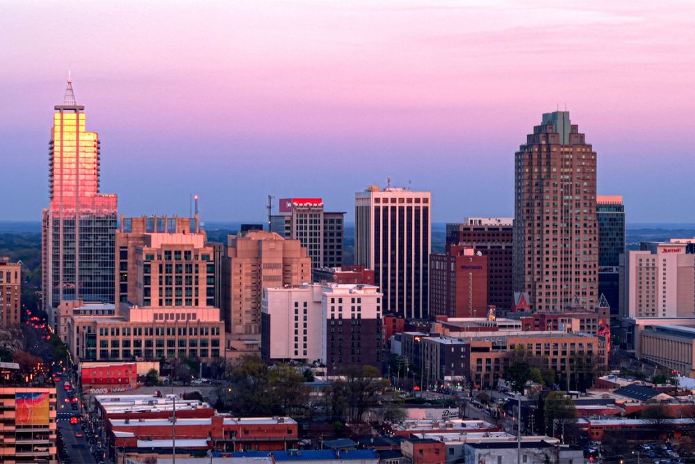 City skyline of Raleigh, North Carolina, at sunset under a purple and pink sky.